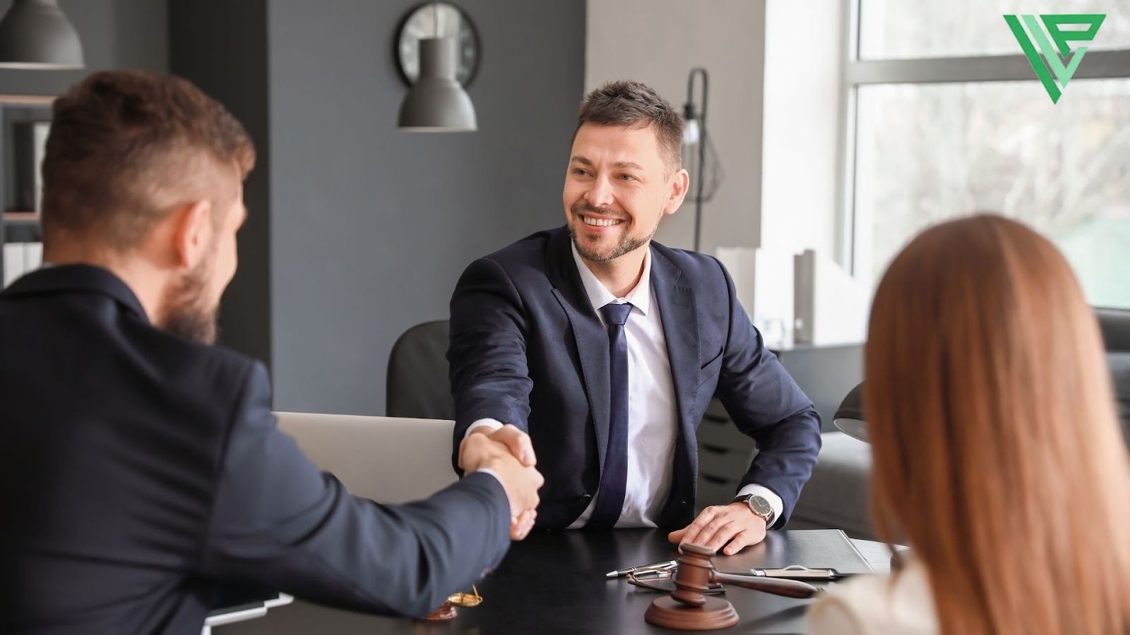 A lawyer shakes the hand of a client from across the table, celebrating their compensation win from a motorcycle hazard case. A red headed client is also present. 