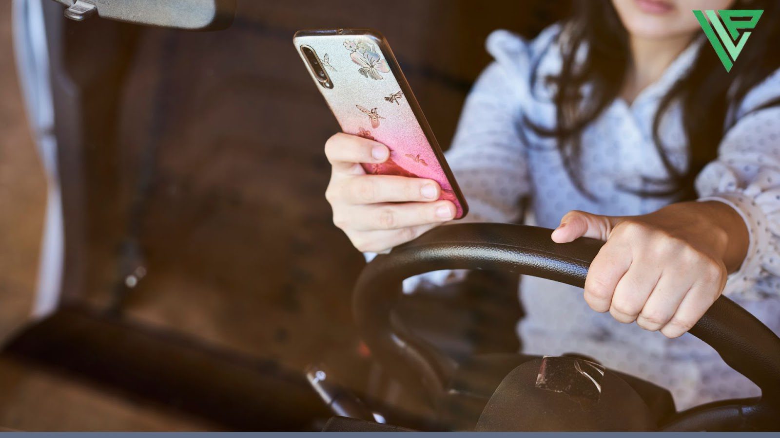 A close-up of hands holding both a steering wheel and a smartphone with a decorative butterfly case, depicting distracted driving behavior.