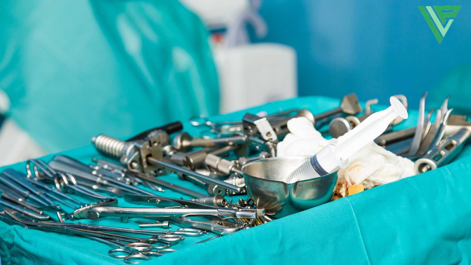 A set of surgical instruments, including forceps, clamps, and a syringe, are laid out on a sterile table covered with a green surgical drape in an operating room, about to be used on a victim of a car accident.
