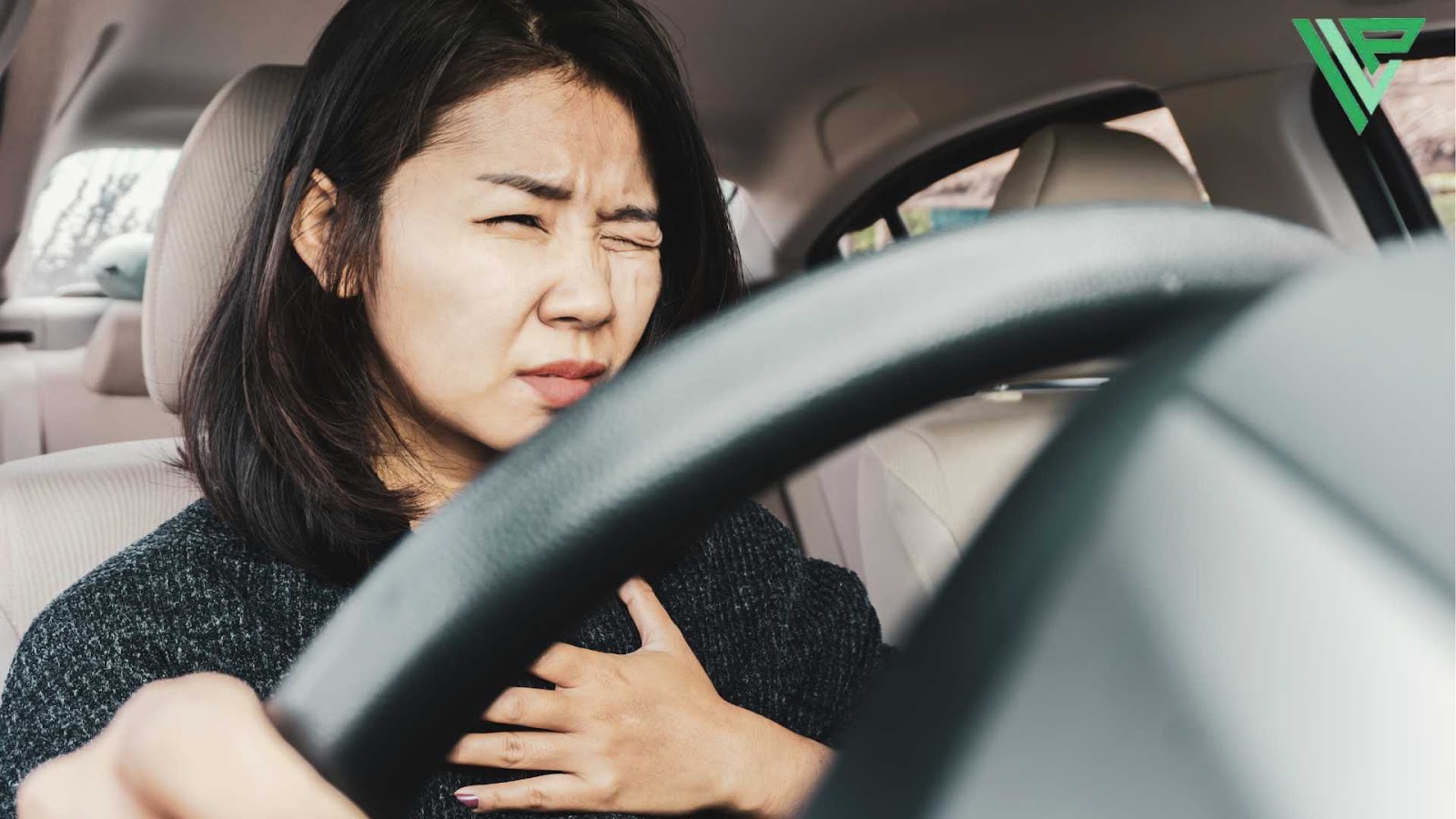 A woman is seated in the driver’s seat, one hand on the steering wheel and the other pressed against her chest. Her eyes are partially closed, and she appears to be experiencing discomfort suggesting that she is dealing with medical issue while driving.