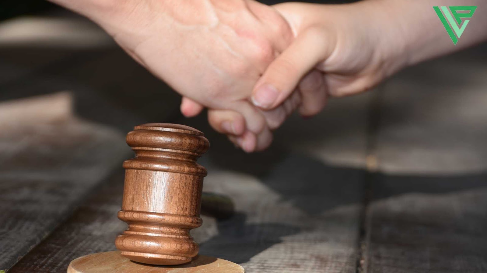 A wooden judge’s gavel rests on a table while two hands shake over an uber lawsuit settlement. 