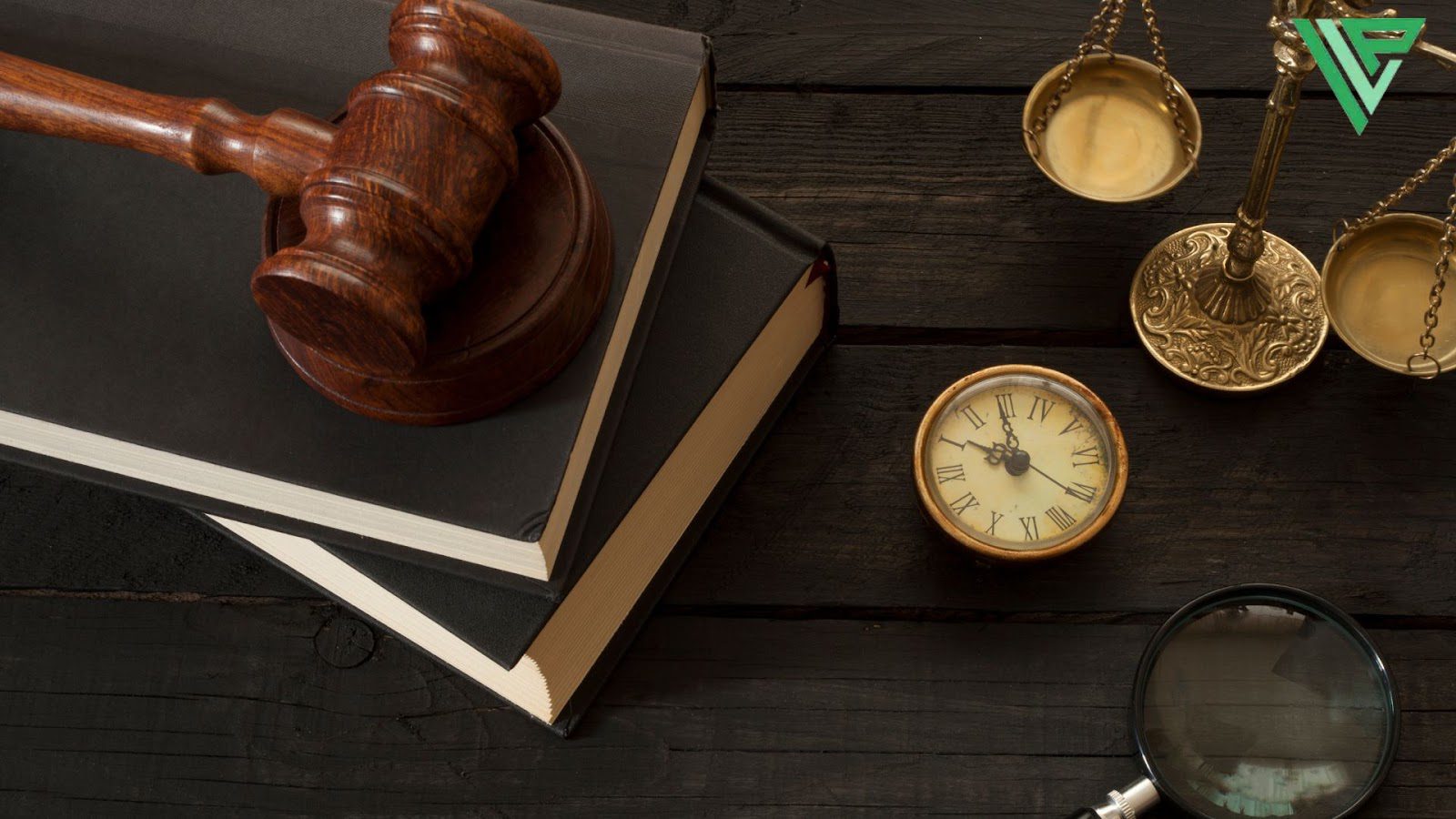 A wooden judge's gavel rests on law books alongside vintage items including a brass scale of justice, an antique clock, and a magnifying glass, all arranged on a dark wooden surface.