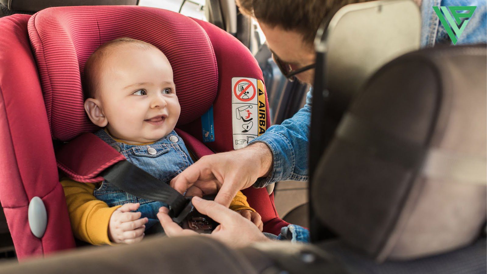 A baby is seen smiling and getting buckled into a red front facing car seat by a man.